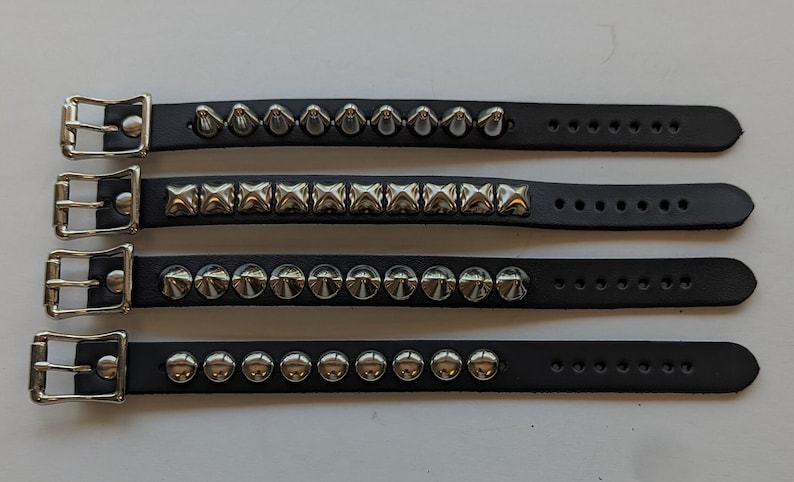 May include: Four black leather bracelets with silver studs. The bracelets have different styles of studs, including pyramid, square, and round.