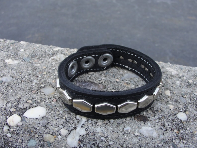 May include: Black leather bracelet with silver hexagonal studs and three silver snap closures.