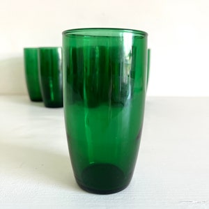 May include: Set of four green glass tumblers. The tumblers are clear and have a slightly rounded shape.