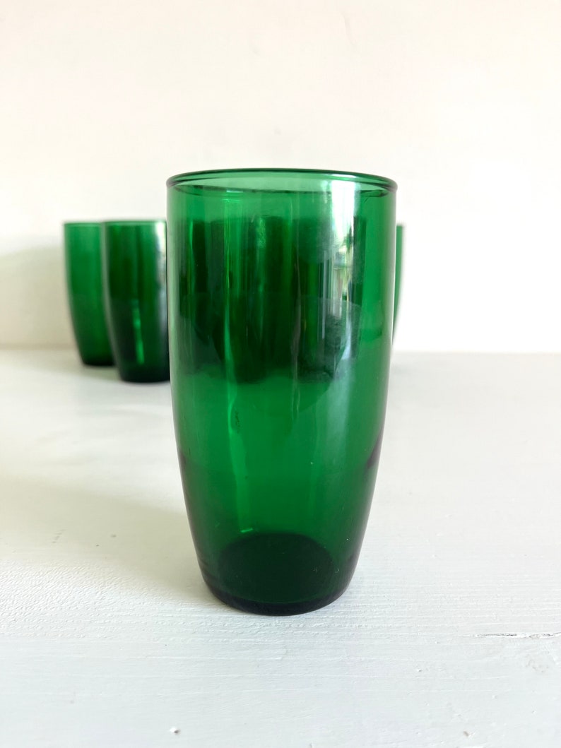 May include: Set of four green glass tumblers. The tumblers are clear and have a slightly rounded shape.