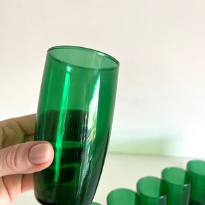 May include: A set of seven green glass tumblers. The tumblers are all the same size and shape, and they have a smooth, rounded bottom.