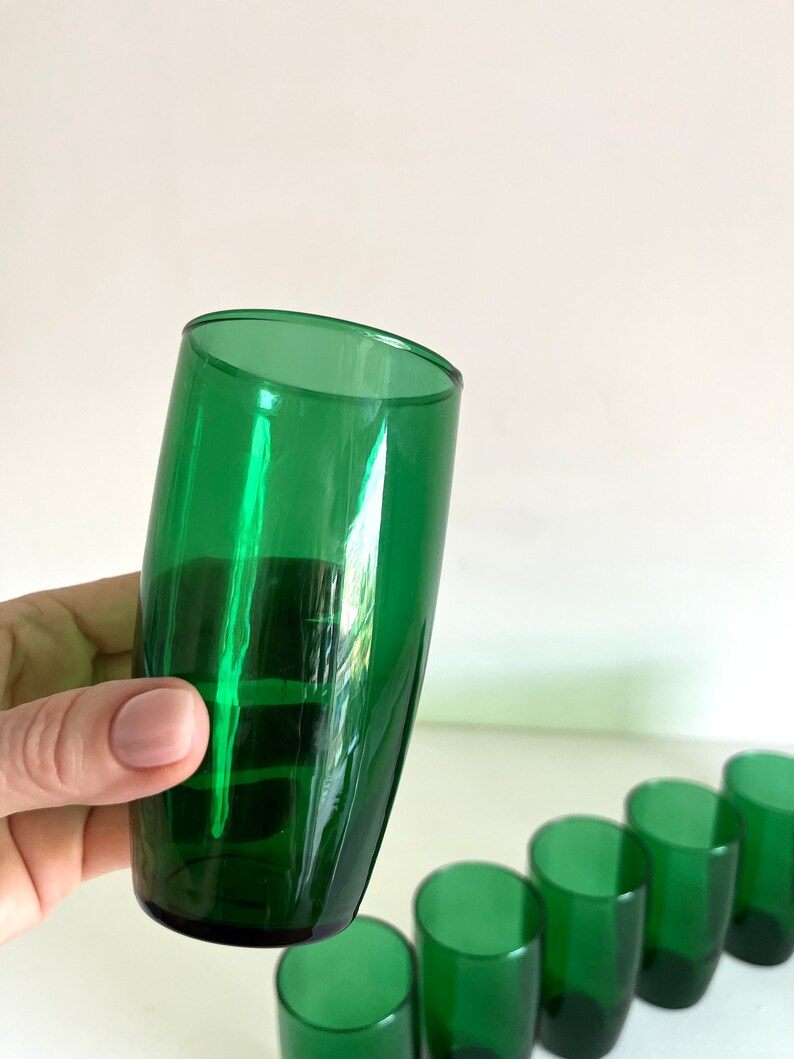 May include: A set of seven green glass tumblers. The tumblers are all the same size and shape, and they have a smooth, rounded bottom.