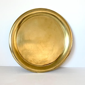 Peut inclure: Un plateau rond en laiton doré avec un bord légèrement surélevé. Le plateau a une surface lisse et réfléchissante et une couleur chaude et invitante. Le plateau est idéal pour servir ou exposer des objets.