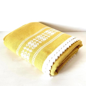 Peut inclure: Couverture jaune pliée avec des motifs géométriques blancs et une bordure en dentelle blanche. La couverture est faite d'une matière douce et est pliée soigneusement. Le design comprend une série de formes géométriques blanches.