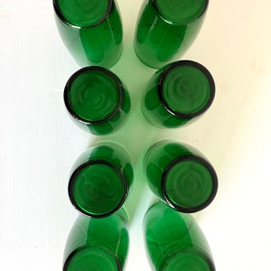 May include: Set of eight green glass tumblers, viewed from above. The glasses are empty and have a smooth, rounded rim.