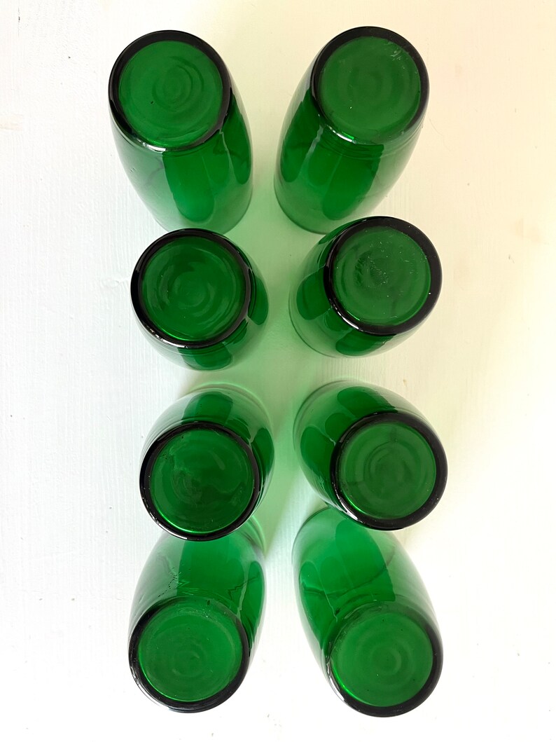 May include: Set of eight green glass tumblers, viewed from above. The glasses are empty and have a smooth, rounded rim.
