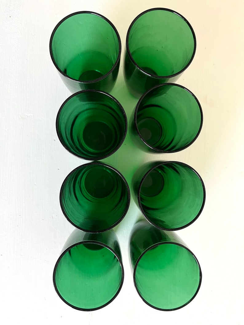May include: Eight green glass tumblers, arranged in two rows of four, on a white surface.