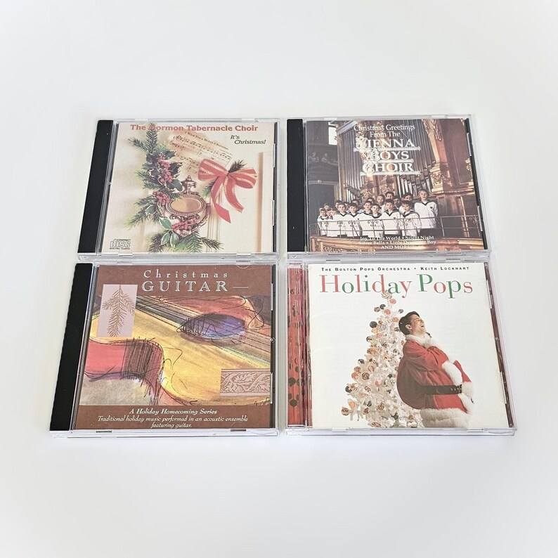 K&ouml;nnte beinhalten: Vier CDs mit Weihnachtsmotiven. Die CDs zeigen Bilder von einem Weihnachtsbaum, einem Chor, einer Gitarre und einem Weihnachtsmann. Die Titel der CDs lauten "The Mormon Tabernacle Choir", "Christmas Greetings from the Vienna Boys Choir", "Christmas Guitar" und "Holiday Pops".