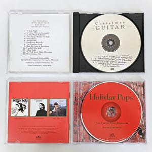 K&ouml;nnte beinhalten: Vier CD-H&uuml;llen mit Weihnachtsmusik. Die H&uuml;llen sind wei&szlig;, schwarz und rot. Die Discs tragen die Titel "Christmas - Guitar", "Holiday Pops" und "Boston Pops".
