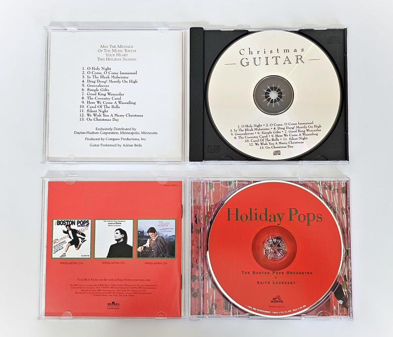 K&ouml;nnte beinhalten: Vier CD-H&uuml;llen mit Weihnachtsmusik. Die H&uuml;llen sind wei&szlig;, schwarz und rot. Die Discs tragen die Titel "Christmas - Guitar", "Holiday Pops" und "Boston Pops".