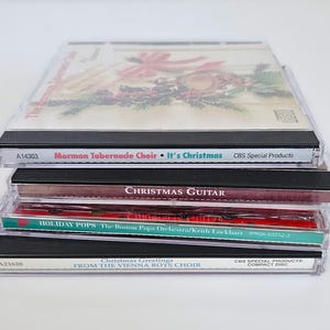 K&ouml;nnte beinhalten: Ein Stapel von vier Weihnachts-Musik-CDs. Die oberste CD zeigt ein rotes und gr&uuml;nes Weihnachtsdesign mit dem Text "Mormon Tabernacle Choir It's Christmas CBS Special Products". Die zweite CD hat den Text "CHRISTMAS GUITAR". Die dritte CD hat den Text "HOLIDAY POPS The Boston Pops Orchestra/Keith Lockhart". Die unterste CD hat den Text "Christmas Greetings FROM THE VIENNA BOYS CHOIR CBS SPECIAL PRODUCTS COMPANY DISC".