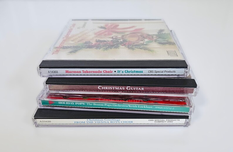 K&ouml;nnte beinhalten: Ein Stapel von vier Weihnachts-Musik-CDs. Die oberste CD zeigt ein rotes und gr&uuml;nes Weihnachtsdesign mit dem Text "Mormon Tabernacle Choir It's Christmas CBS Special Products". Die zweite CD hat den Text "CHRISTMAS GUITAR". Die dritte CD hat den Text "HOLIDAY POPS The Boston Pops Orchestra/Keith Lockhart". Die unterste CD hat den Text "Christmas Greetings FROM THE VIENNA BOYS CHOIR CBS SPECIAL PRODUCTS COMPANY DISC".