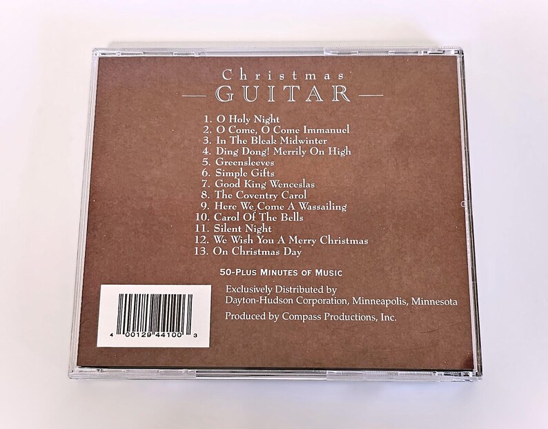 K&ouml;nnte beinhalten: Ein braunes CD-Geh&auml;use mit einem wei&szlig;en Etikett, auf dem "Christmas Guitar" steht und 13 Weihnachtslieder aufgelistet sind. Das Etikett enth&auml;lt auch einen Barcode und den Text "50-Plus Minutes of Music".