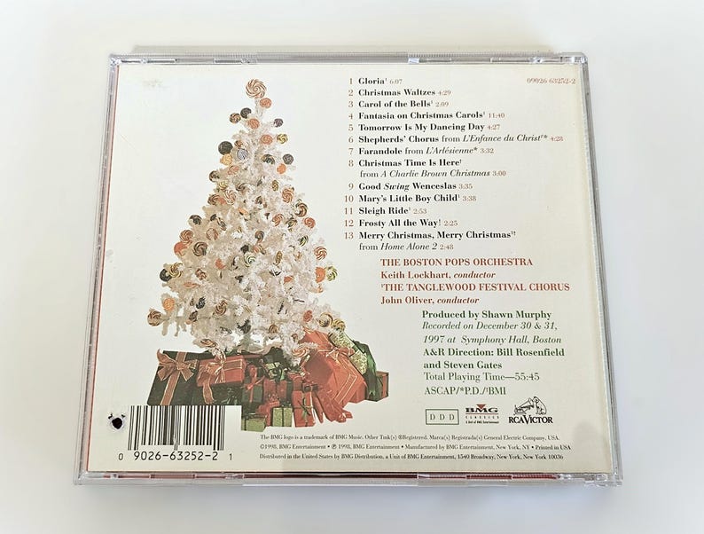 K&ouml;nnte beinhalten: Ein CD-Geh&auml;use mit einem wei&szlig;en Weihnachtsbaum auf der Vorderseite und einer Liste von Weihnachtsliedern auf der R&uuml;ckseite. Die R&uuml;ckseite enth&auml;lt auch Informationen &uuml;ber die K&uuml;nstler, das Boston Pops Orchestra und den Tanglewood Festival Chorus, sowie die Aufnahmedetails.