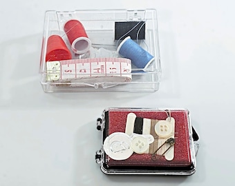 May include: Two clear plastic containers with sewing supplies. The first container has two red spools of thread, a blue spool of thread, and a small measuring tape. The second container has a red felt lining with two white buttons, a small spool of thread, a safety pin, and a needle.