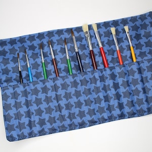 Könnte beinhalten: Eine blaue Stoff-Pinselrolle mit Sternenmuster. Die Rolle hat 10 Fächer für Pinsel.