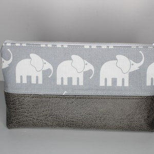Könnte beinhalten: Eine graue Reißverschlusstasche mit einem grauen und weißen Elefantenmuster. Die Tasche hat einen braunen Kunstlederboden und einen Reißverschluss mit einem Anhänger, auf dem "Kindergeschenk" steht.