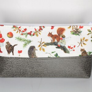 Könnte beinhalten: Eine weiße Reißverschlusstasche mit grauem Boden. Die Tasche hat einen verspielten Wald-Druck mit einem Eichhörnchen, Igel, Katze und einem Mädchen in einem roten Kleid. Der Druck enthält auch Beeren, Blätter und Kiefernäste. Der Reißverschluss hat einen kleinen Anhänger mit dem Text "Kleidereckchen".