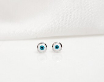 May include: A pair of silver stud earrings with a blue and white evil eye design.