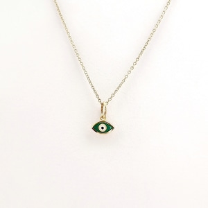 May include: A delicate gold necklace featuring a small pendant in the shape of an eye. The eye pendant has a green center and a white iris, set in a gold frame. The necklace is displayed against a white background.