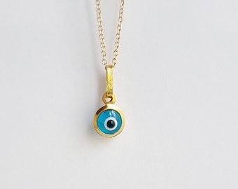 May include: A gold chain necklace with a blue evil eye pendant. The pendant is round and has a white center.