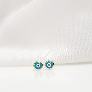 Könnte beinhalten: Ein Paar goldene Ohrringe mit blauen und weißen bösen Augen.