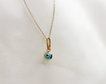 May include: A gold chain necklace with a small blue evil eye pendant.