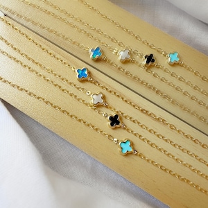 Puede incluir: Cinco collares de cadena de oro con dijes de trébol de diferentes colores. Los dijes son turquesa, blanco, negro, turquesa y blanco.