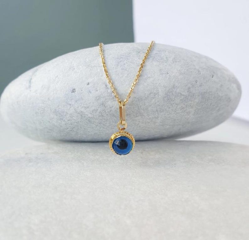 Pu&ograve; includere: Una collana con catena d'oro con un ciondolo blu a forma di occhio turco. Il ciondolo &egrave; circondato da una cornice dorata.