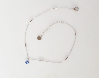 Könnte beinhalten: Ein silbernes Fußkettchen mit einem blauen bösen Augen-Anhänger und einem herzförmigen Anhänger. Das Fußkettchen hat eine zarte Kette mit kleinen silbernen Stäben.
