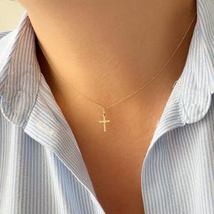 Può includere: Una collana con catena d'oro e un piccolo ciondolo a forma di croce d'oro.