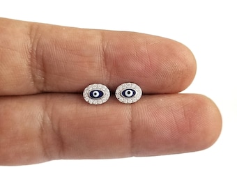 May include: A pair of silver earrings with a blue evil eye design and a clear crystal halo around each eye.