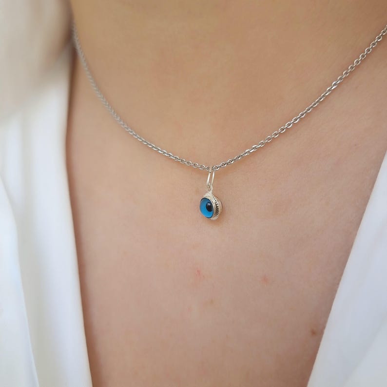 Pu&ograve; includere: Una collana con catena d'argento con un piccolo ciondolo blu a forma di occhio.