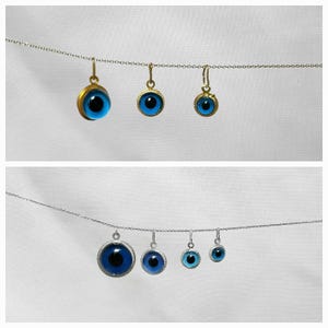 Pu&ograve; includere: Un set di cinque ciondoli con occhio blu maligno su catene d'argento e d'oro. I ciondoli sono di diverse dimensioni e sono tutti rotondi con un bordo dorato.
