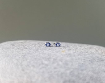 May include: A pair of silver stud earrings with blue and white evil eye charms.
