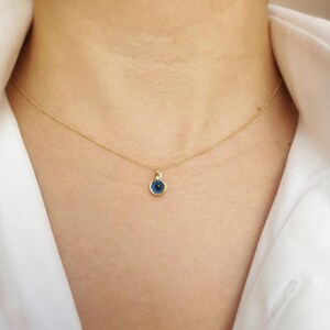 Pu&ograve; includere: Una collana con catena dorata con un piccolo ciondolo blu a forma di occhio turco. Il ciondolo &egrave; rotondo e ha un bordo dorato.