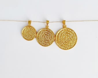 May include: Three gold-colored pendant necklaces with circular, textured designs. The pendants are suspended from a thin, gold-colored chain against a white background. The pendants vary in size, with the largest on the right.