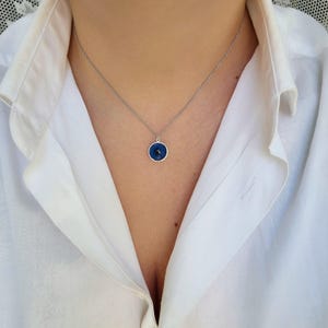 Pu&ograve; includere: Una collana con catena d'argento con un ciondolo blu a forma di occhio turco. Il ciondolo &egrave; rotondo e ha un bordo bianco.