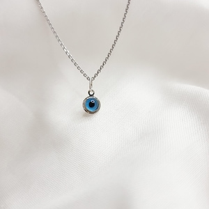 Pu&ograve; includere: Una collana con catena d'argento con un ciondolo blu a forma di occhio turco. Il ciondolo &egrave; rotondo e ha un bordo argentato.