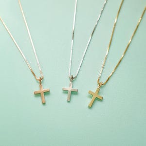 Può includere: Tre collane con croci in oro rosa, argento e oro, ciascuna sospesa a una sottile catena. Le croci sono semplici ed eleganti, su uno sfondo verde chiaro. Un classico design di gioielli religiosi.