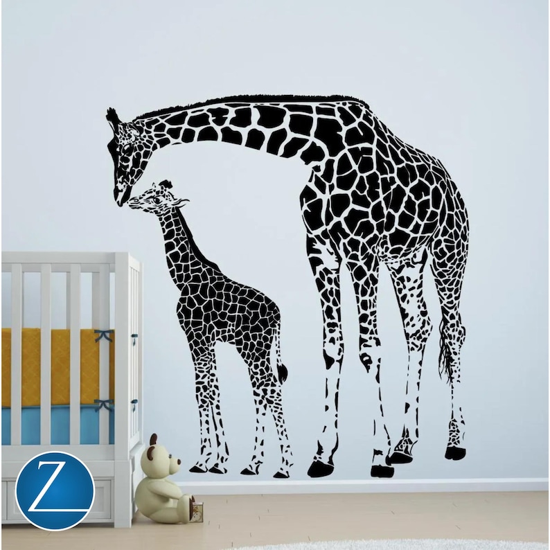 Black vinyl wall decal of a mother giraffe touching heads with her baby giraffe, displayed on a nursery wall beside a crib and stuffed bear.