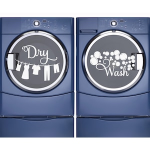 May include: Two dark blue laundry appliances featuring white vinyl decals on their circular glass doors. The left unit displays the word Dry with a clothesline graphic, while the right unit shows the word Wash with a cluster of bubbles.