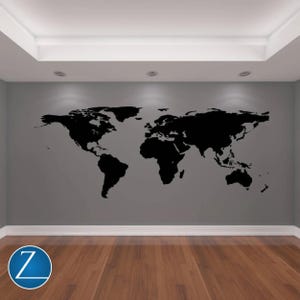 May include: A large black world map decal is affixed to a gray wall. The map is a silhouette of the continents and oceans. The room has a wooden floor and recessed lighting.