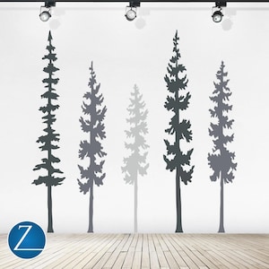 May include: A wall decal set featuring five tall, slender pine tree silhouettes in varying shades of gray, ranging from dark charcoal to light gray, arranged vertically against a plain white wall above a light-colored wooden floor.