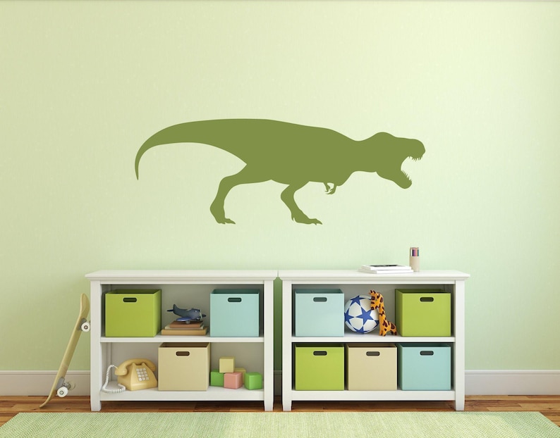 Green T. rex silhouette wall decal displayed on a light green wall above toy storage shelves in a dinosaur-themed kids room.