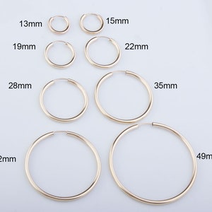 May include: A set of six gold hoop earrings in various sizes, ranging from 13mm to 49mm in diameter. The earrings are arranged in order of size, with the smallest on the left and the largest on the right.