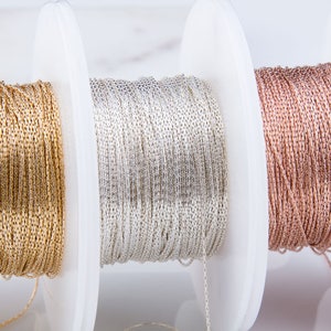 May include: Three spools of metallic cord, one gold, one silver, and one rose gold. The cord is wound around white spools.