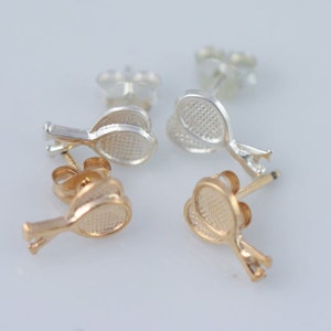 Puede incluir: Un par de pendientes con un diseño de raqueta de tenis. Un par es de plata y el otro es de oro.