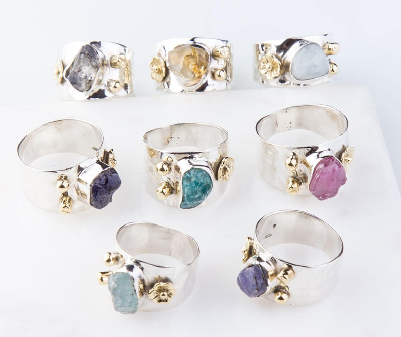 May include: Ten silver rings with different colored gemstones. Each ring has a textured band and gold accents. The gemstones include amethyst, aquamarine, citrine, emerald, ruby, and topaz.