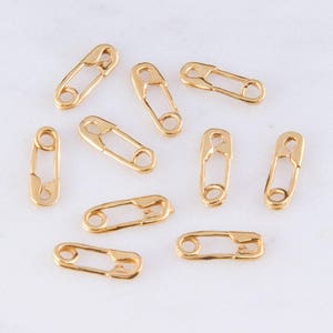 May include: Ten gold-toned safety pins, each with a simple design. These pins are small and delicate, perfect for adding a touch of whimsy to jewelry or crafts.